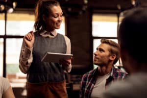 Smiling waitress talking to customers and using touchpad while t
