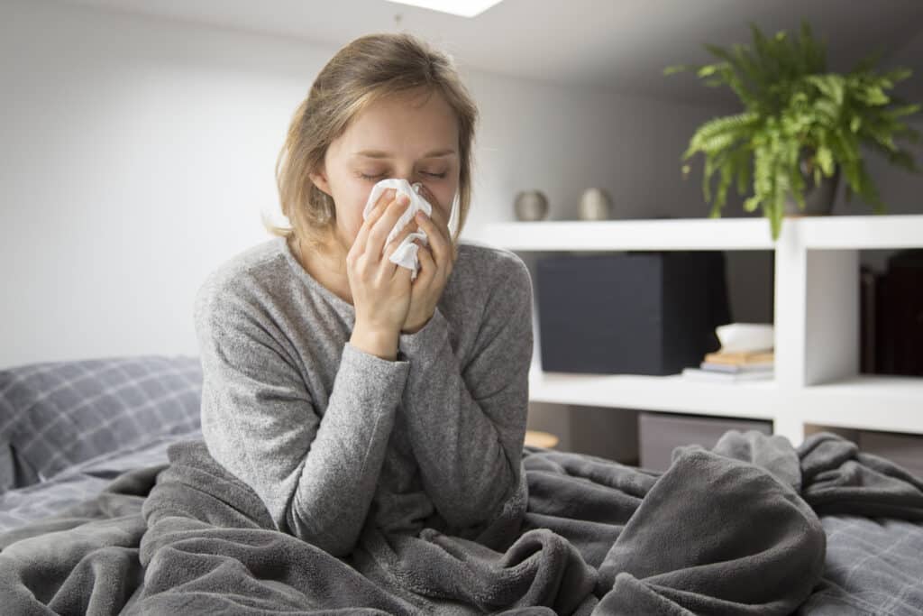 Sick woman sitting in bed, blowing nose with napkin